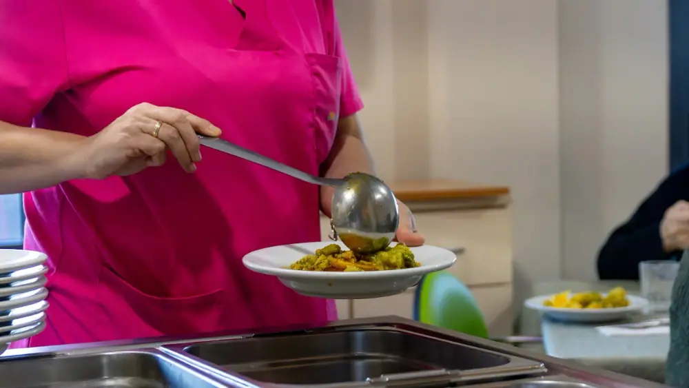 Una cocinera sirve un plato de comida casera en la cocina de Mejora Avilés