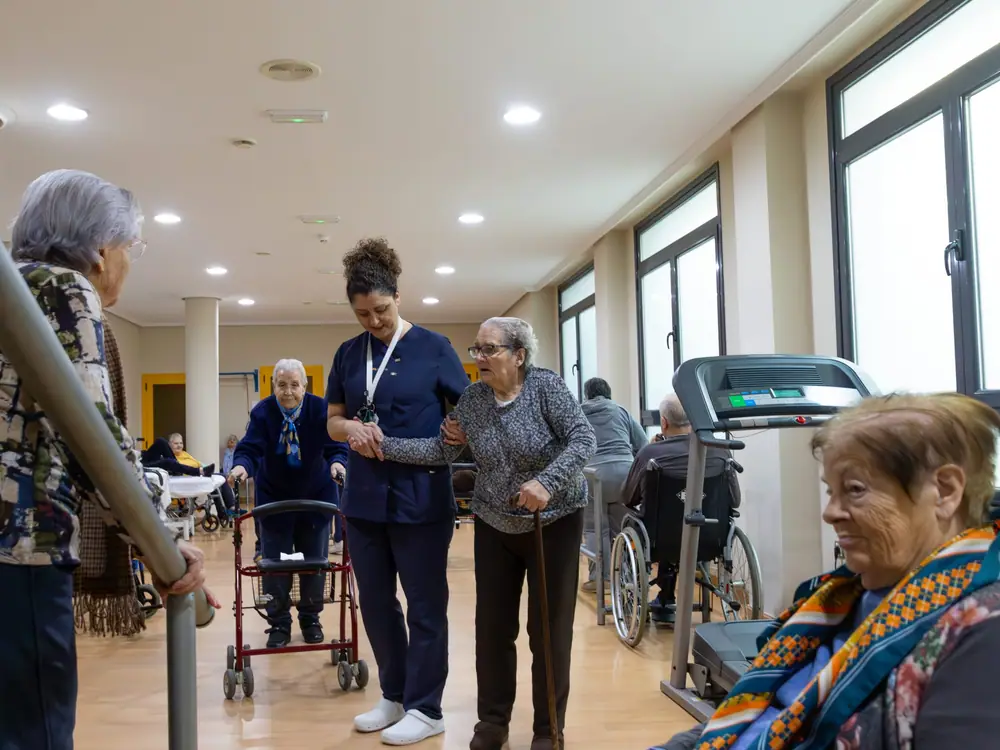 Una residente camina con andador acompañada por una fisioterapeuta en la sala de rehabilitación