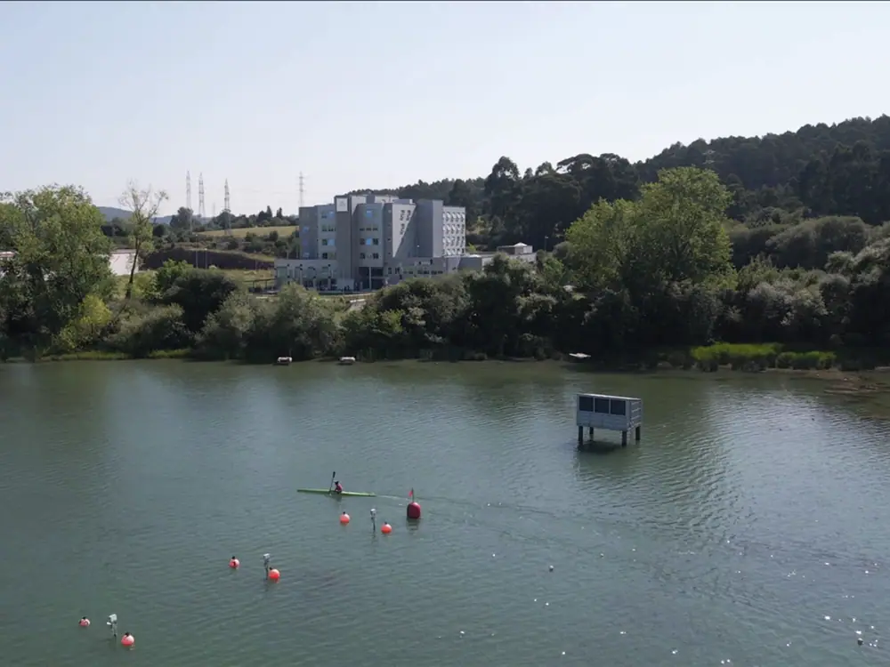 El edificio de Mejora Avilés visto desde el embalse de Trasona, con las calles de remo en primer plano